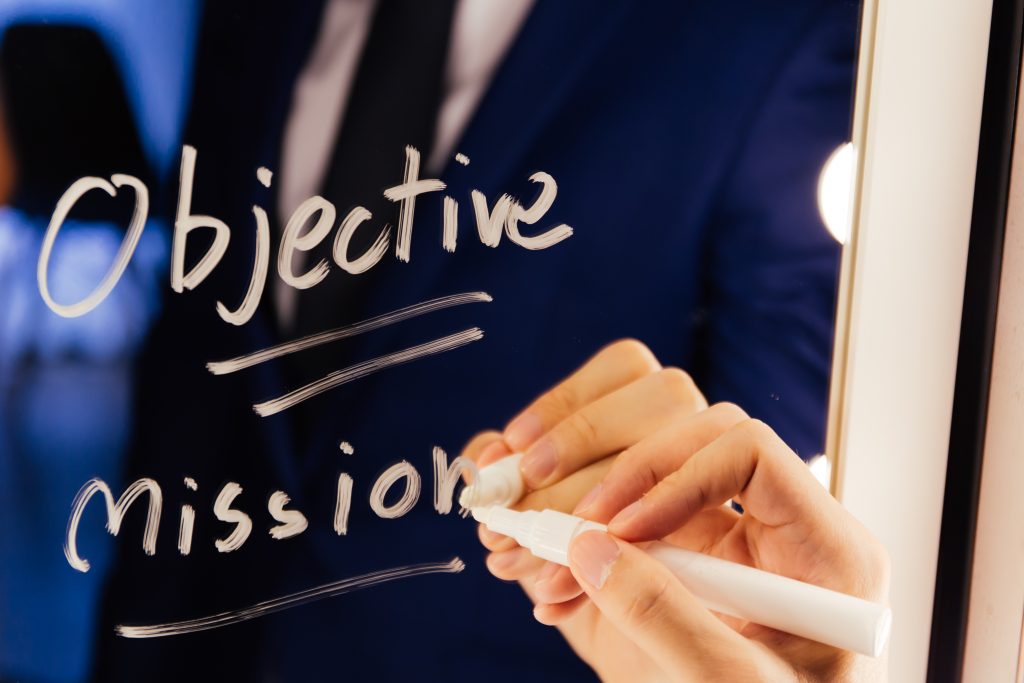 person writing Objective and Mission on glass