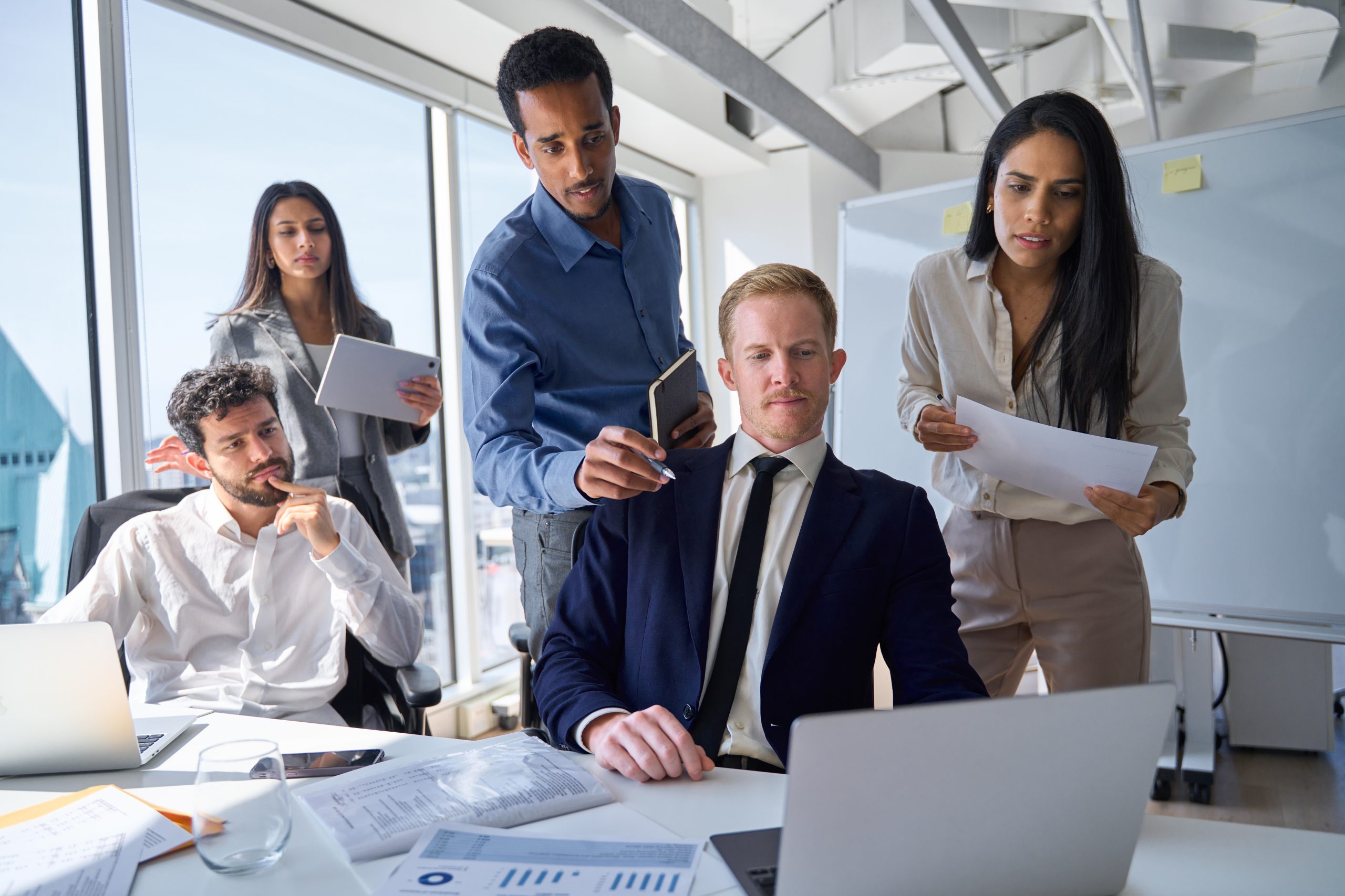 Busy diverse professional business people board executives looking at laptop in office. International workers group and team leader having teamwork discussion managing project at work in meeting room.