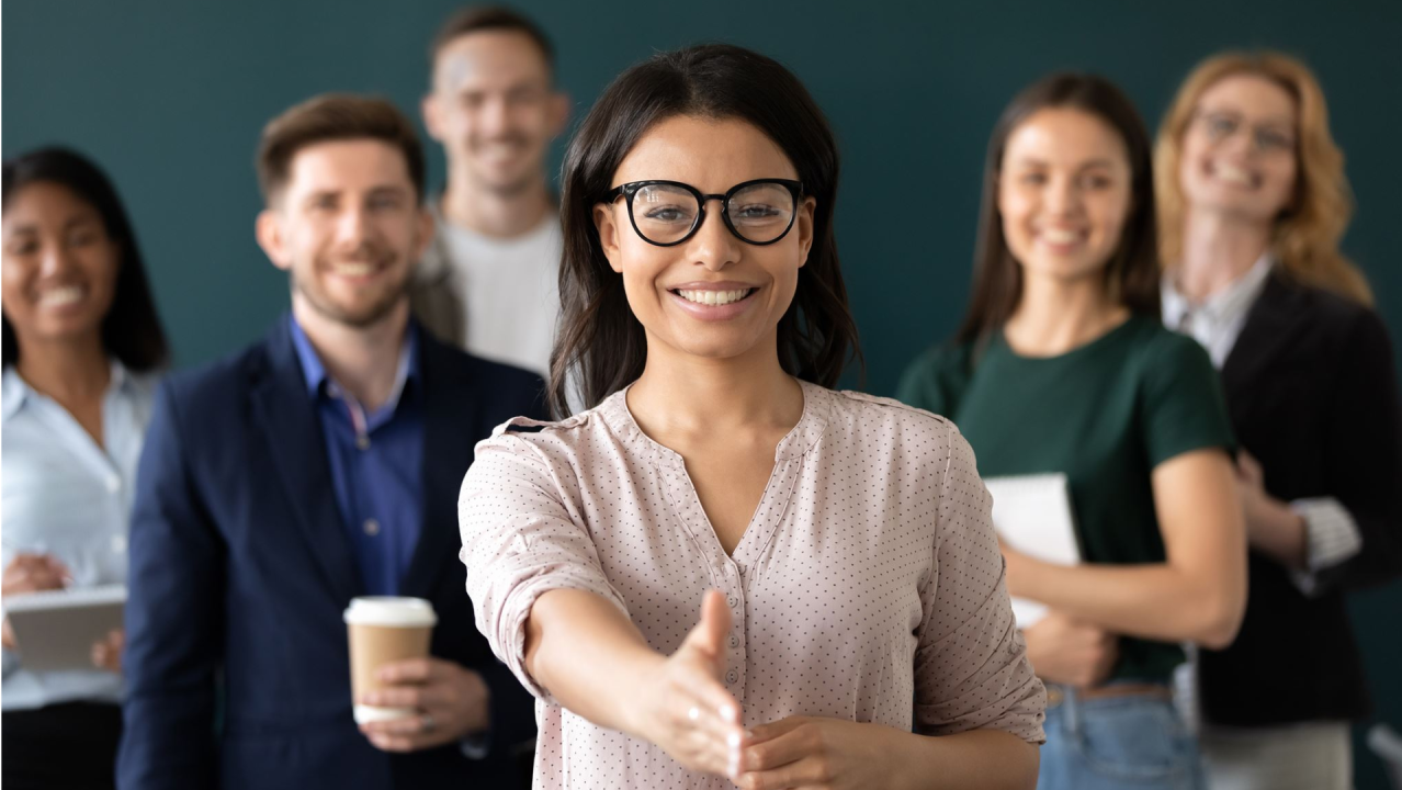 young woman in glasses in front of a group of people holding their hand out for a handshake